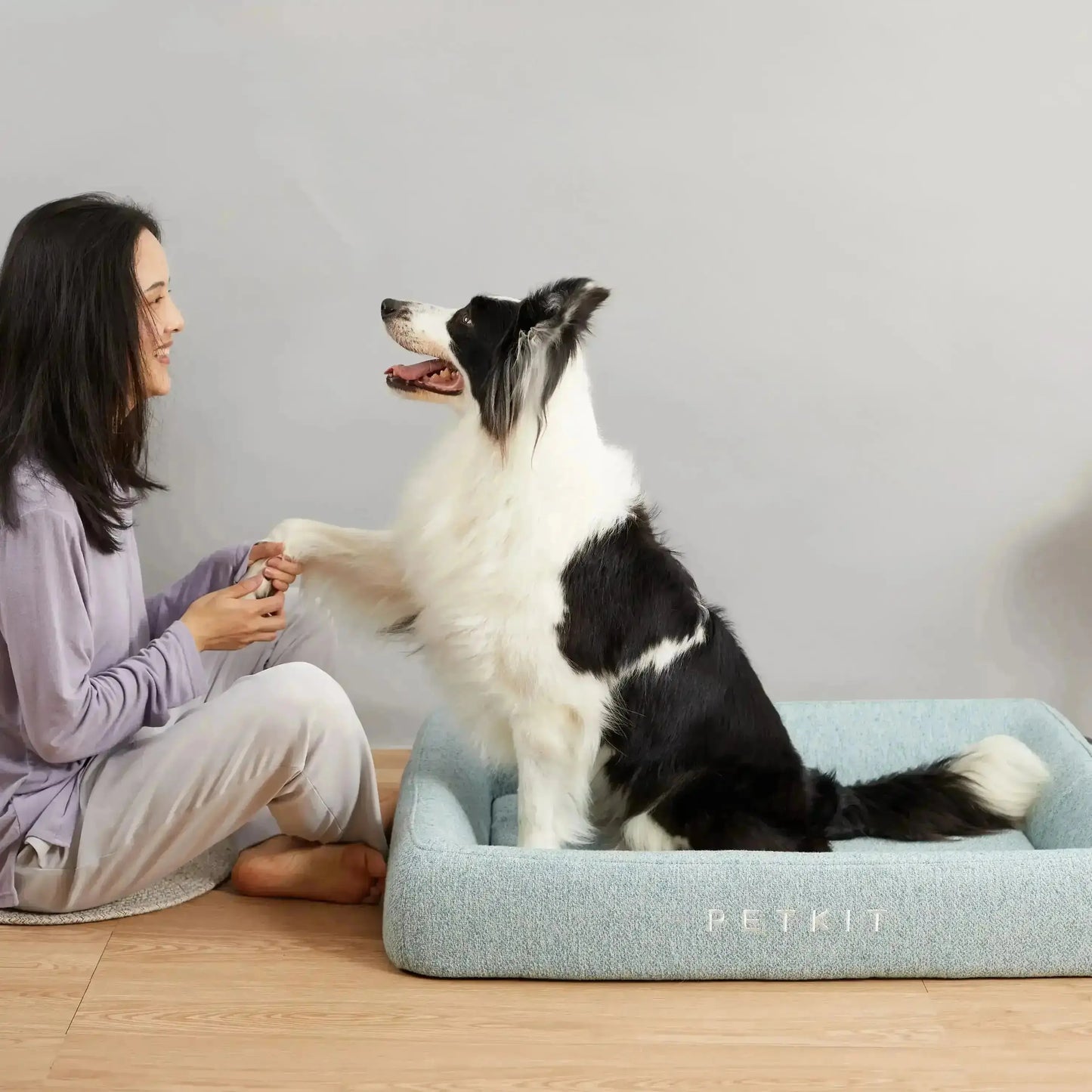 Hond zit in een PETKIT hondenbed naast vrouw, zacht blauw kussen voor comfort en ondersteuning.