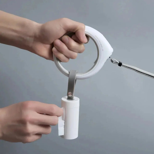 een petkit hondenpoepzakjes container aan een hondenlijn. handig want zo kun je met een hand de hond vast houden en met de ander een zakje uit de container pakken